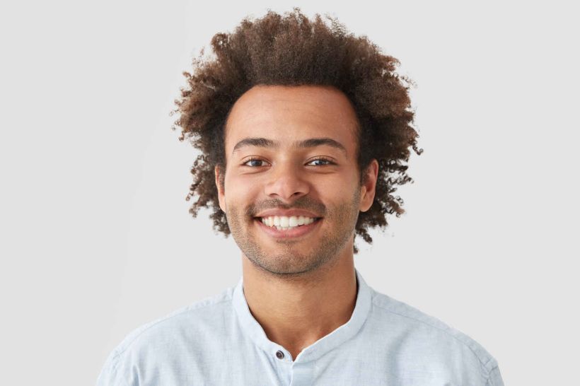 curly-man-with-broad-smile-shows-perfect-teeth-being-amused-by-interesting-talk-has-bushy-curly-dark-hair-stands-indoor-against-white-blank-wall.jpg